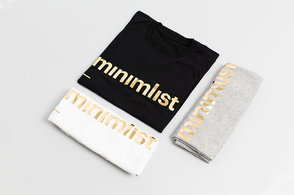Folded t-shirts in black, white, and grey with the golden logotype as frontprint.