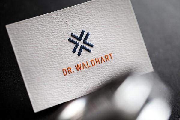 The letterpress business cards with simple white background are printed on a natural paper with a coarse texture.