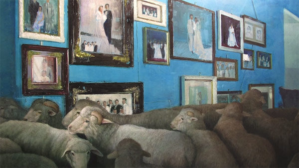 Sheeps in front of a wall of paintings.