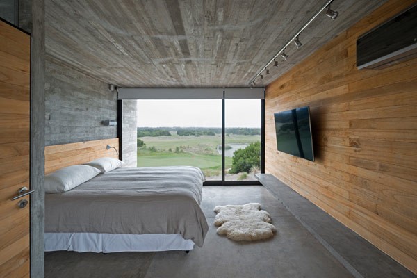 This bedroom has a floor to ceiling window as well as a wood-paneled wall to create a contrast to the concrete walls.