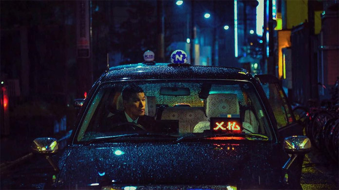 A taxi driver waits in the rain for a couple, which has some fun in the love hotel.